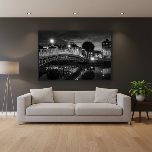 Black and white framed wall art print of the Ha'penny Bridge in Dublin at night. The bridge's historic architecture is beautifully highlighted against the dark sky, with reflections shimmering in the River Liffey below. Ideal for adding elegance to any room or office. Large black and white night-time photograph of Ha’penny Bridge in Dublin with reflections in the Liffey, framed in a black wooden frame, 60x90 cm.